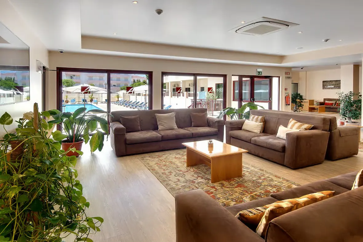 Bright, modern hotel lobby at Hotel Alba in Monte Gordo, Portugal, featuring comfortable lounge seating and large windows overlooking the pool area