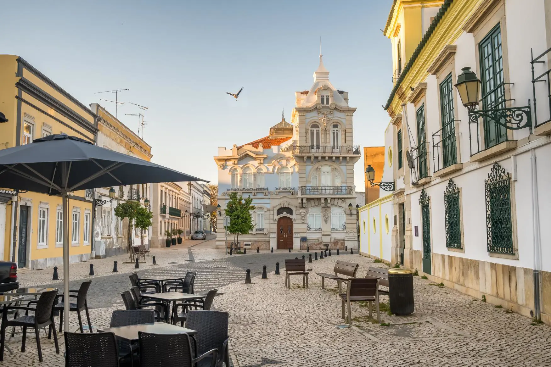 City centre of Faro, Algarve, showing cobbled streets, café tables and benches along the pavement, and Belmarco Palace at the end of the street