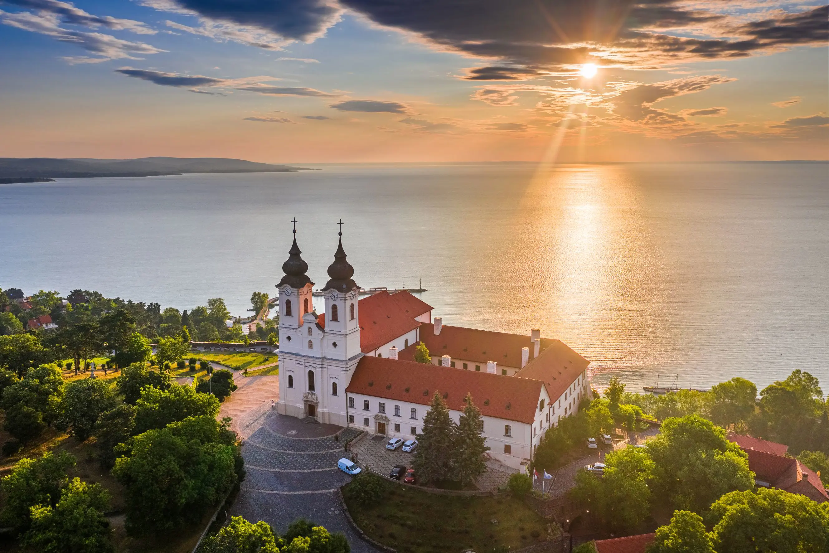 High angle shot of Lake Balaton, with a church with red roofs and two black towers on the waterfront. 
