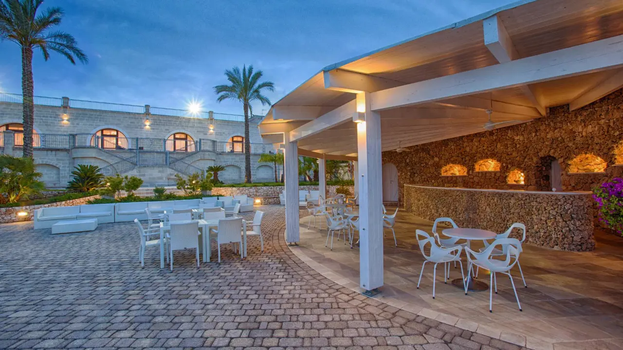 Outdoor dining and bar area at Masseria Caselli Hotel, Italy, with stone walls, white furniture, and warm evening lighting