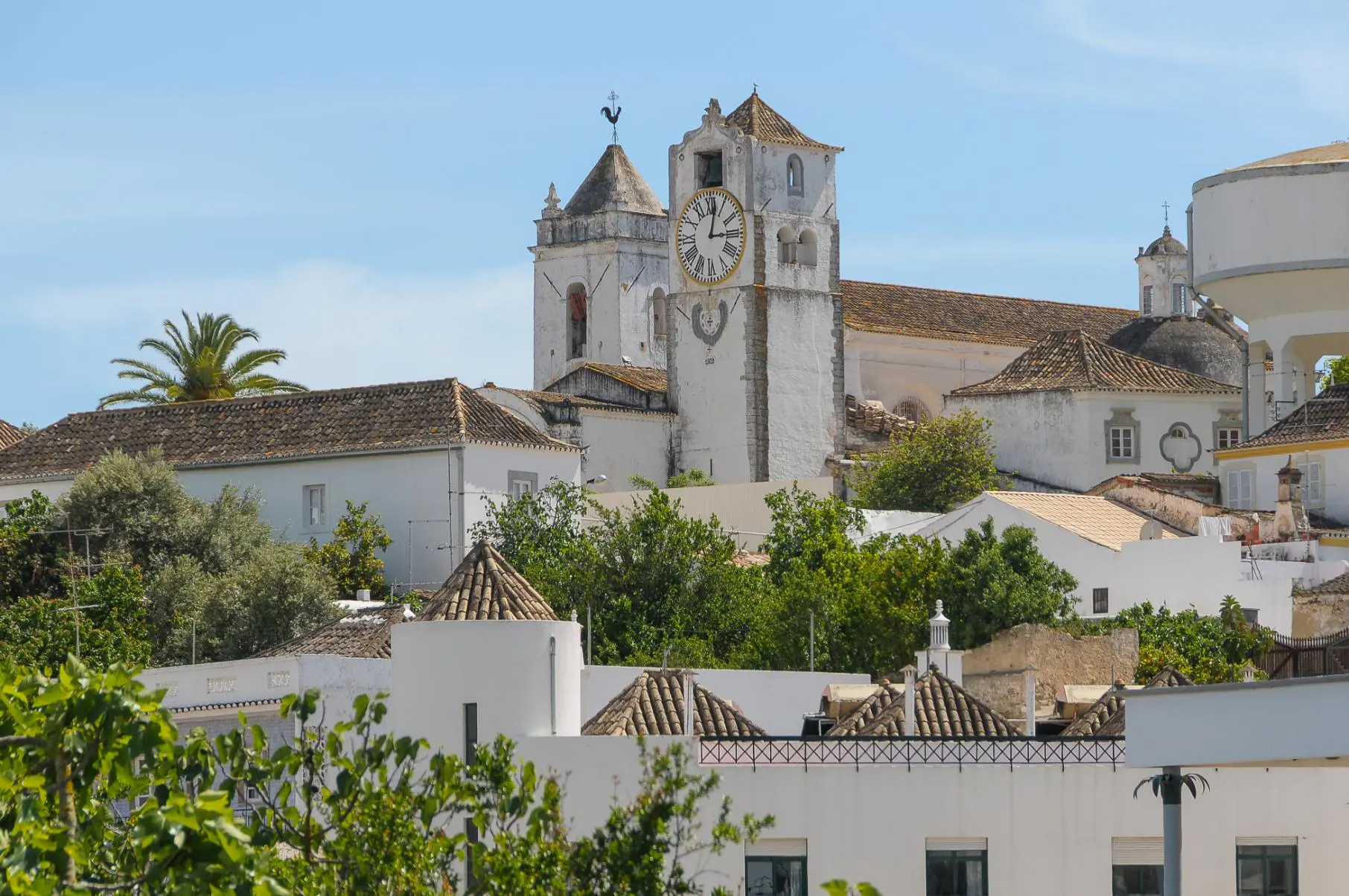Traditional whitewashed clock tower surrounded by trees and town buildings with tiled roofs in Tavira on the Algarve