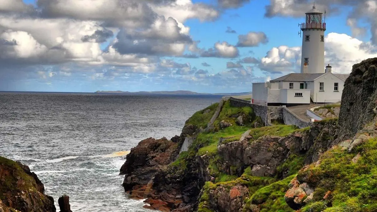 Shot of the coast of Donegal with the Fanad Head Lighthouse on the right, and the sea on the left, with a cloudy but blue sky in the background