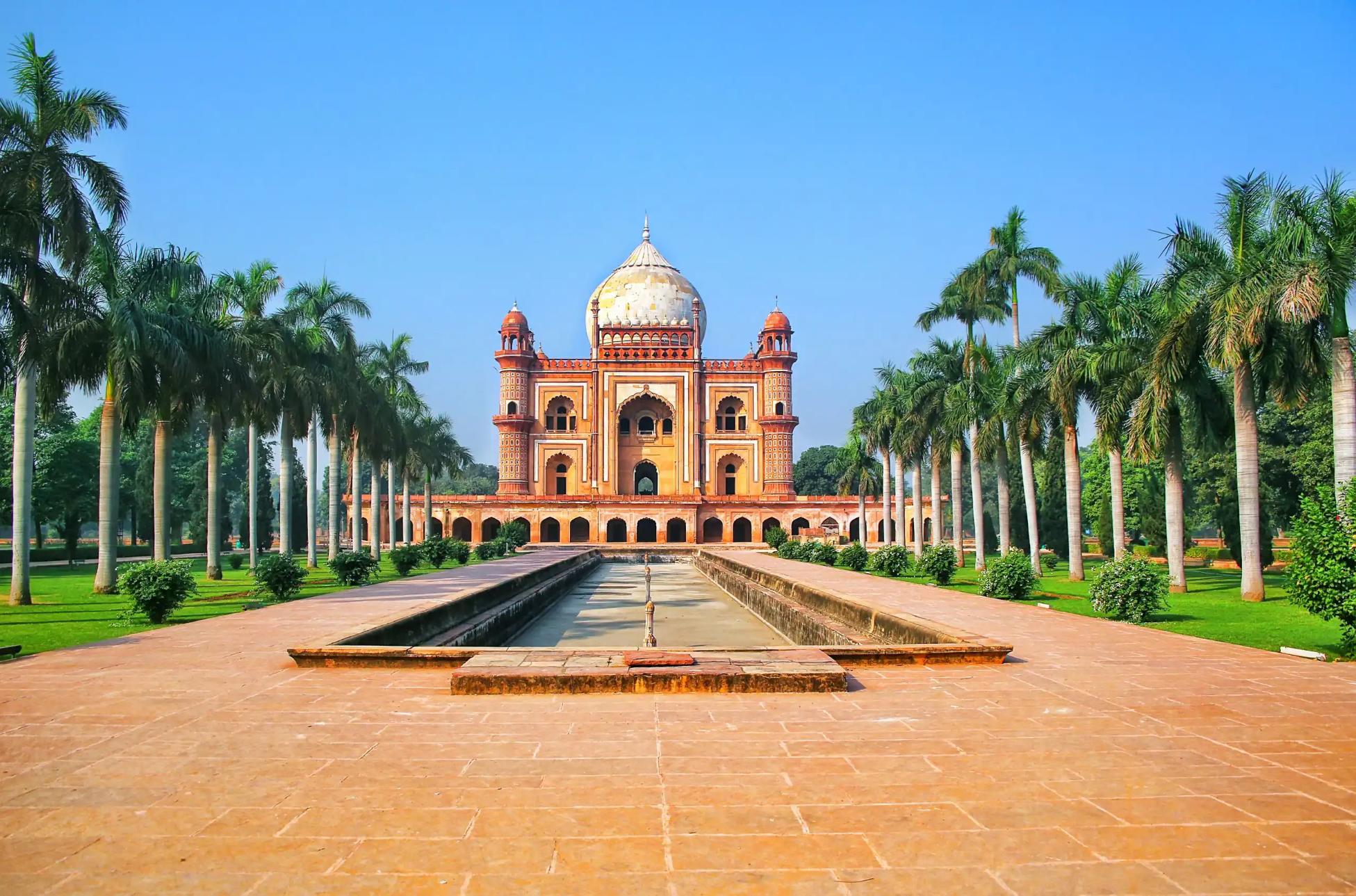 Front view of Humayun's Tomb in Delhi, India, framed by symmetrical rows of palm trees and a long reflecting pool under a clear blue sky