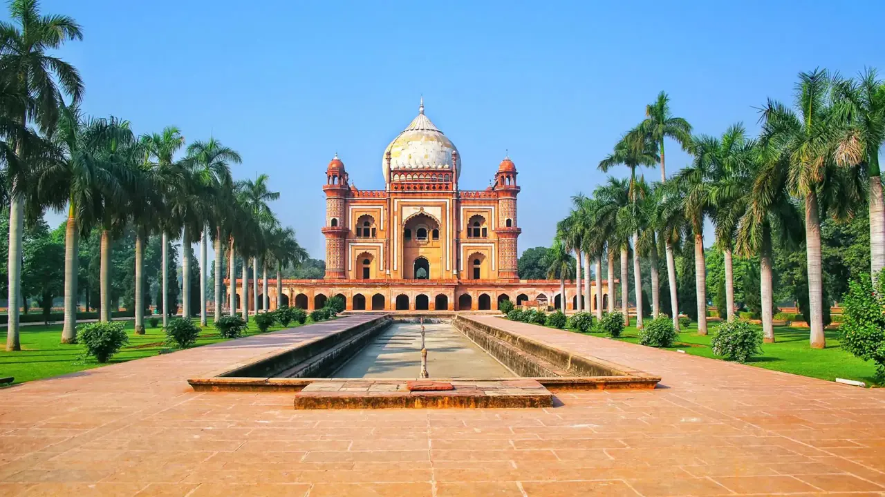 Front view of Humayun's Tomb in Delhi, India, framed by symmetrical rows of palm trees and a long reflecting pool under a clear blue sky