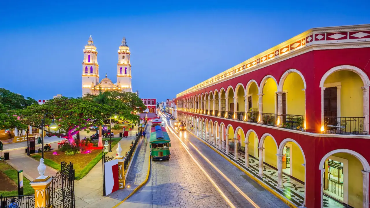 Brightly lit colonial buildings and a cathedral illuminate the street of the historic town of Campeche in Mexico during twilight