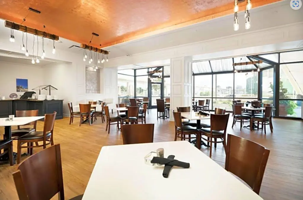 Breakfast area at Fort Pontchartrain hotel, featuring neatly arranged tables and chairs in a bright, spacious dining room with large windows letting in natural light