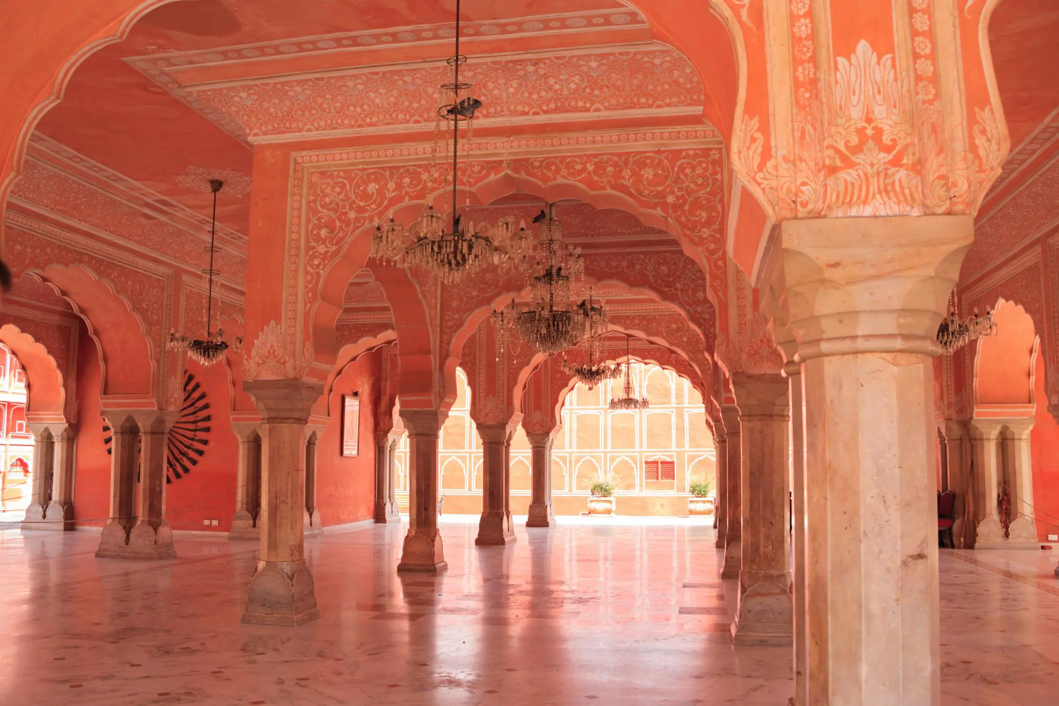 The elegant interior of the City Palace in Jaipur, featuring intricately decorated pink arches, marble floors, and hanging chandeliers under the palace’s domed ceilings