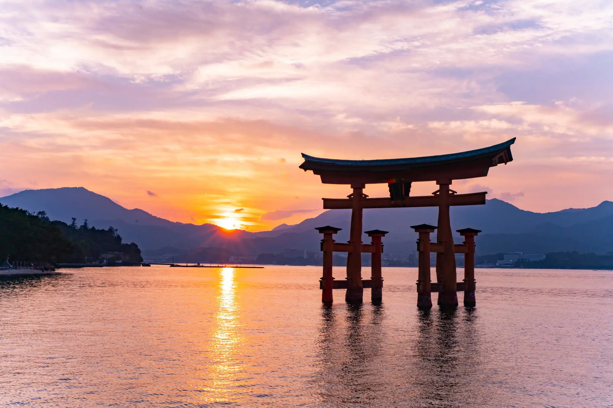 Panoramic view of the beautiful and monumental Floating bridge called Torii of Itsukushima Shrine with a beautiful orange sunset in the background