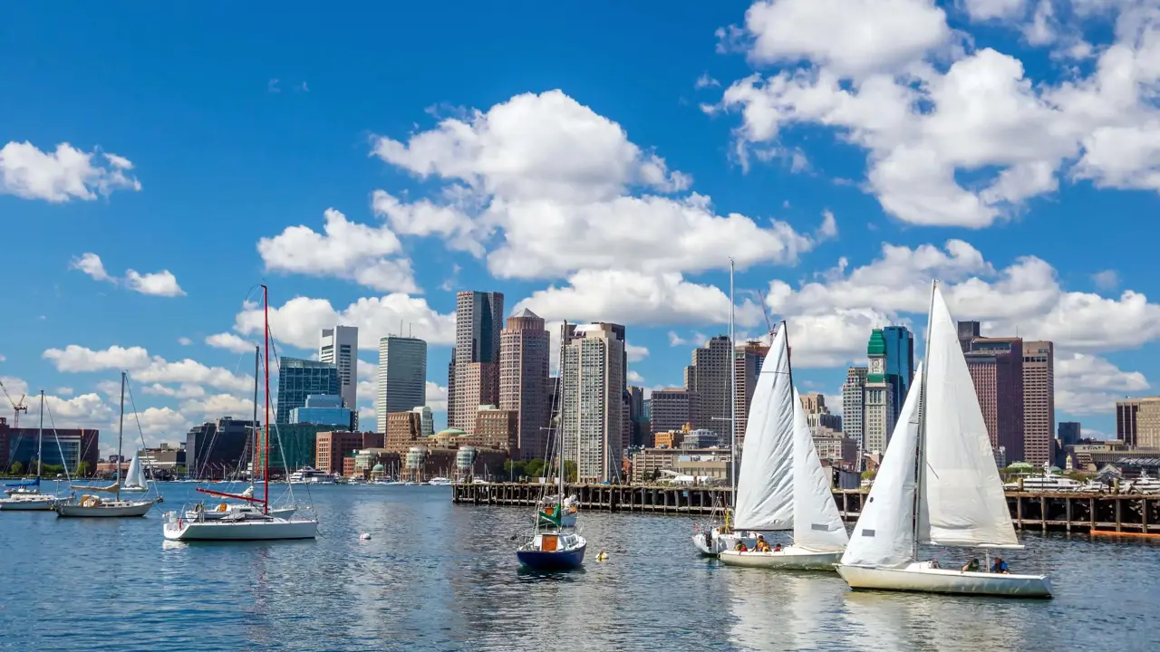 View of Boston, Massachusetts, seen across the water from Pier Park, with the city skyline rising above the harbour under a partly cloudy sky