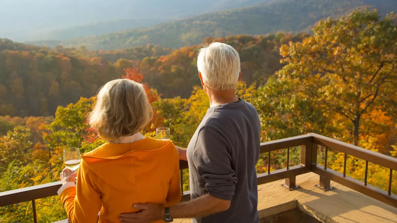 A couple enjoying a glass of wine on a terrace overlooking rolling countryside and colourful trees in New England during autumn