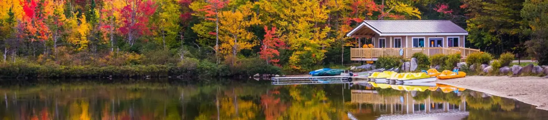A peaceful lake reflects vibrant autumn trees and a cosy wooden cabin with kayaks on the shore in New Hampshire, USA