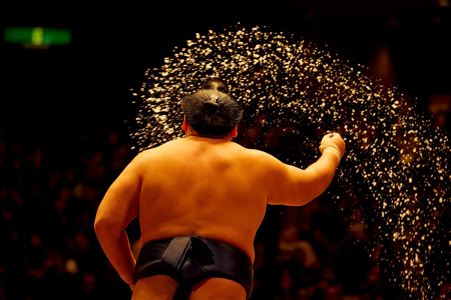 A sumo wrestler viewed from behind, tossing salt into the ring as part of a ritual before a match in Fukuoka, Japan