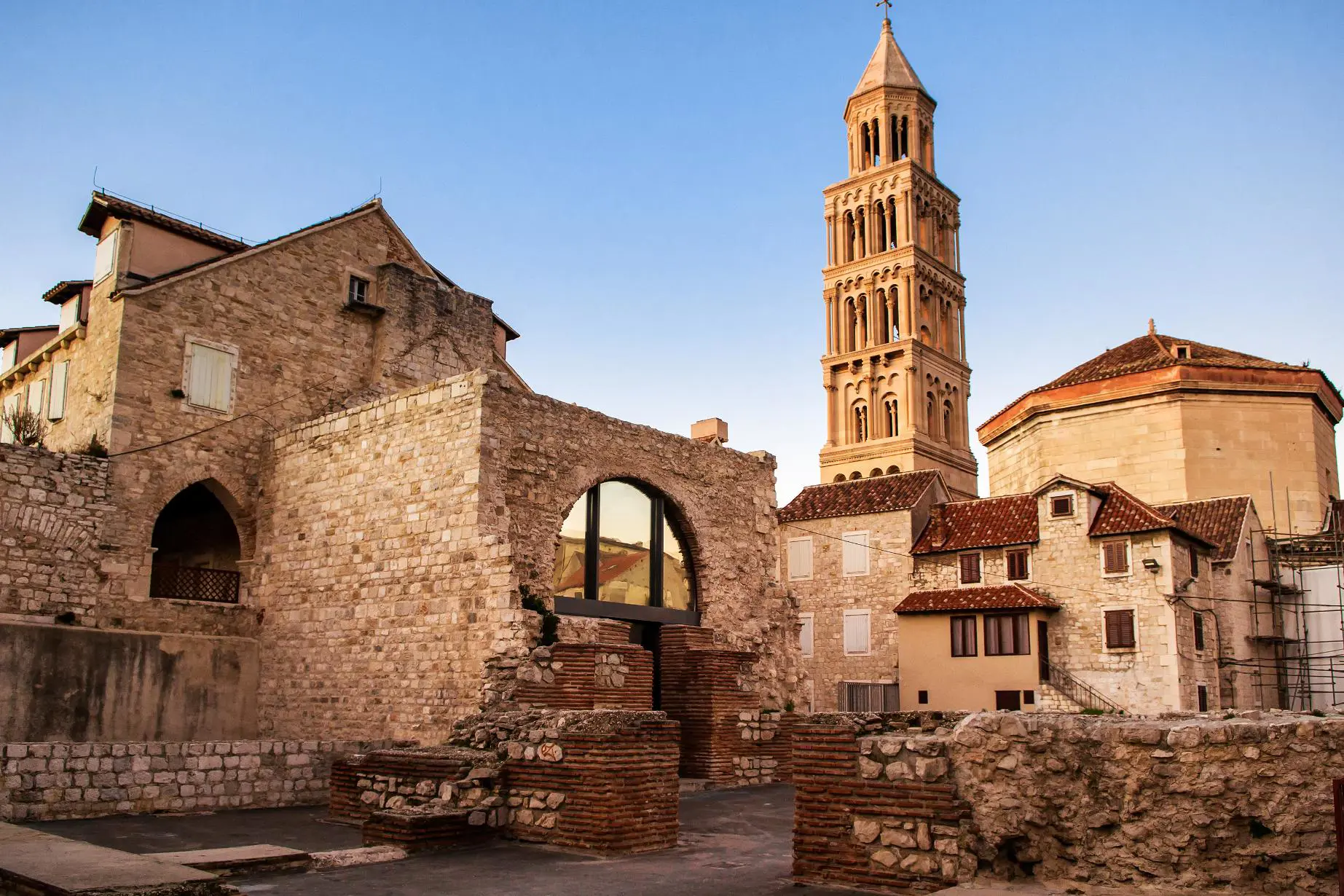 View of St. Domnius Cathedral’s bell tower rising above historic stone houses and ancient Roman ruins in Split’s Old Town, Croatia