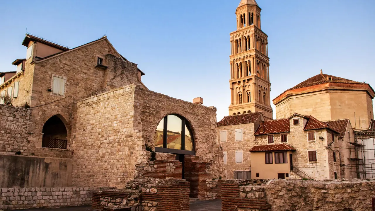 View of St. Domnius Cathedral’s bell tower rising above historic stone houses and ancient Roman ruins in Split’s Old Town, Croatia