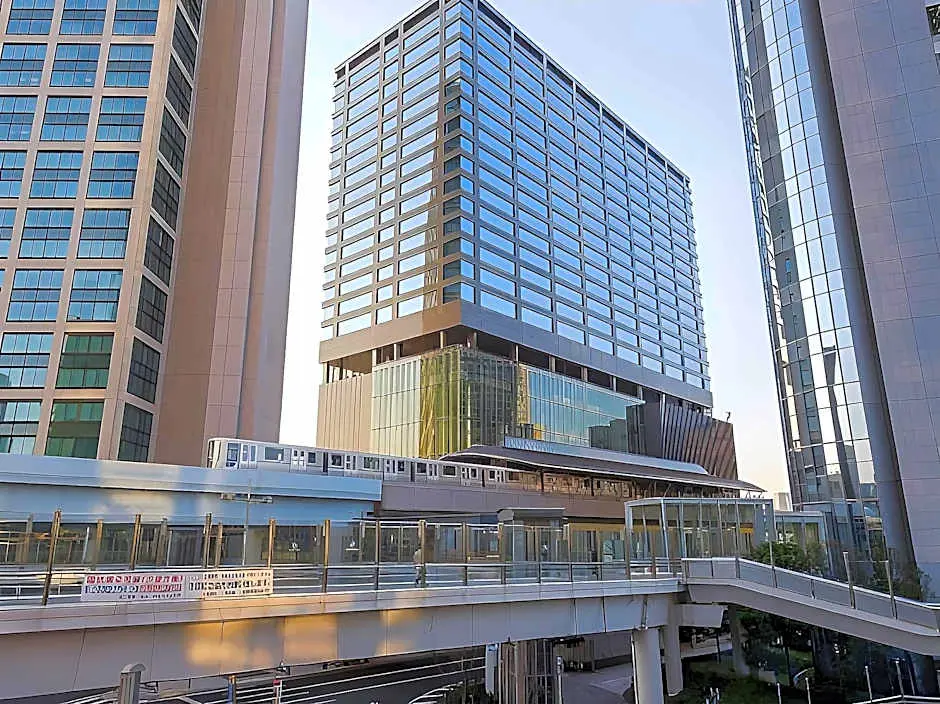 The exterior of Villa Fontaine Grand Tokyo, a modern glass high-rise hotel, with a monorail and skywalk in front