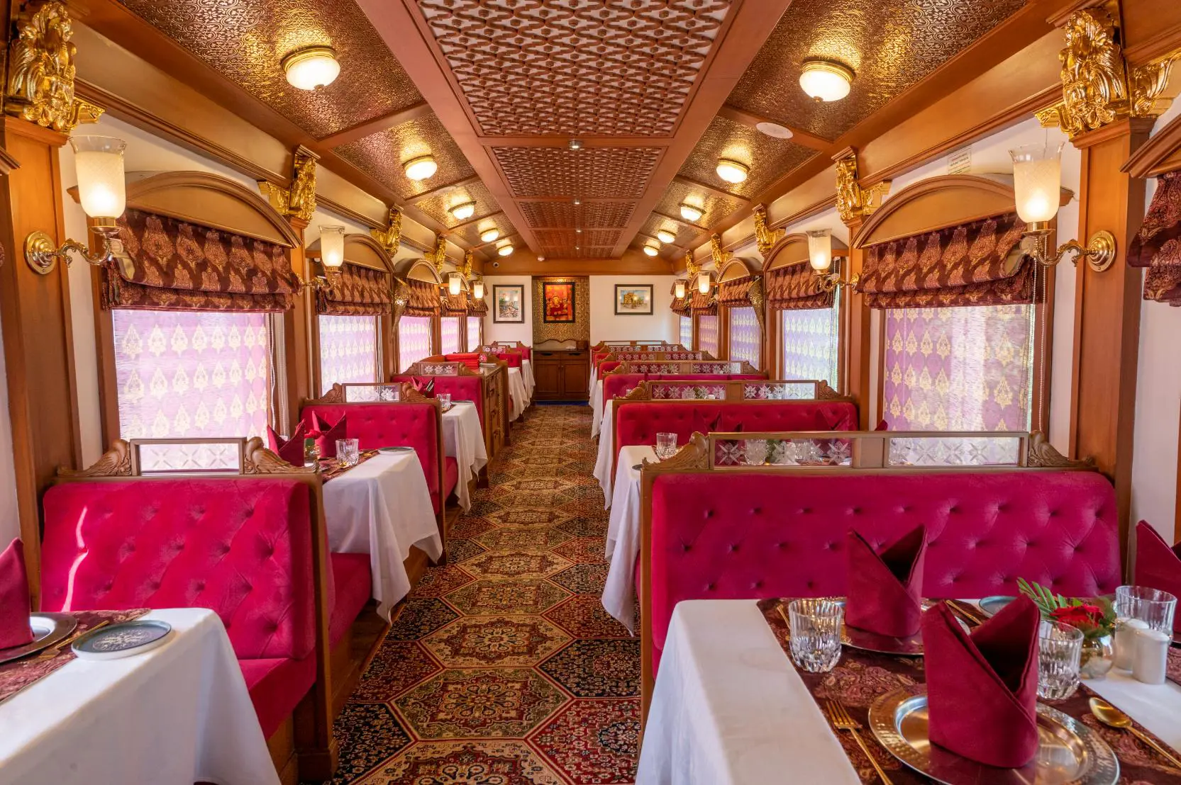 The Deccan Odyssey dining car with red detailing, upholstered seats, patterned curtains, and tables set for meals
