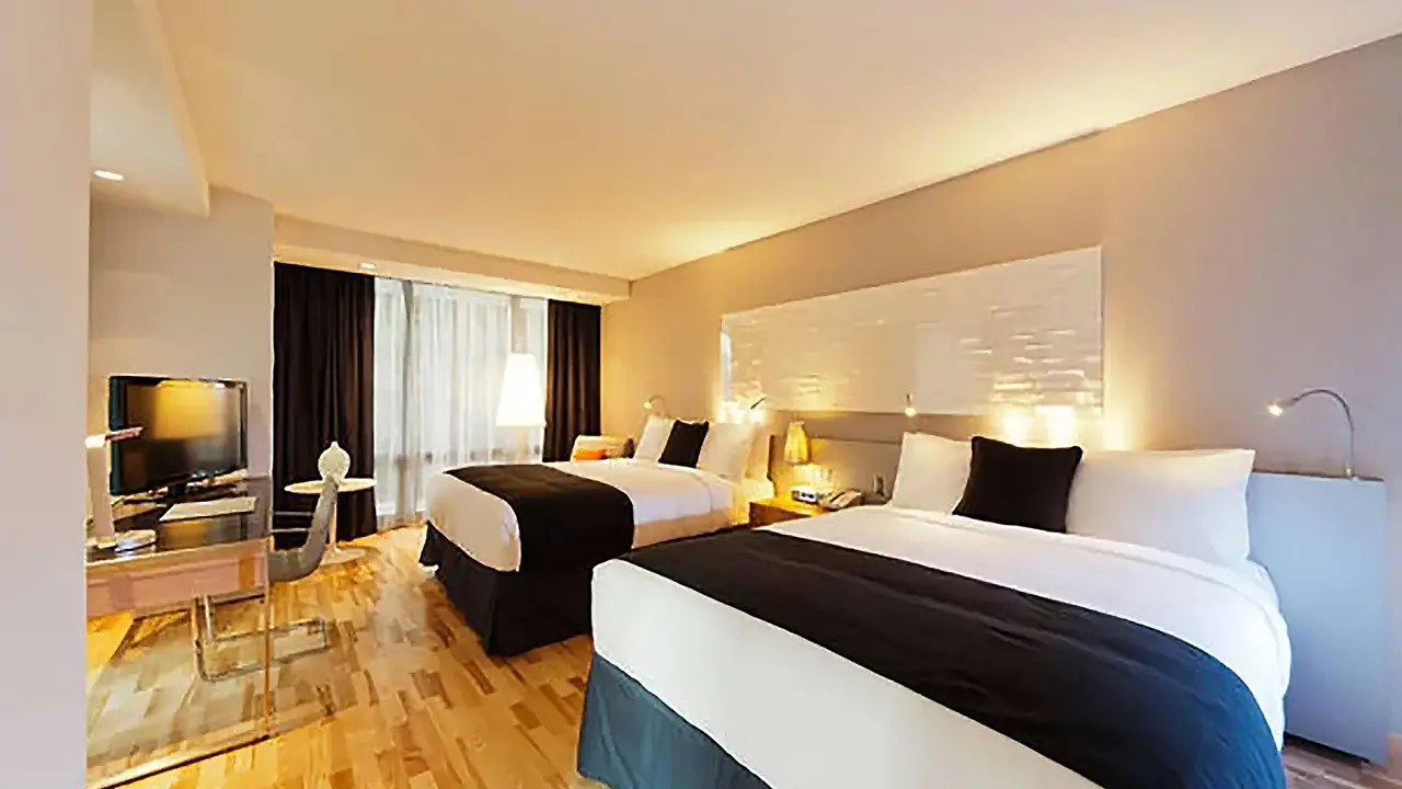 A twin room at Radisson Blu Aqua Hotel, Chicago, featuring two double beds with crisp white linens and a navy bed runner, sleek modern furnishings, floor-to-ceiling windows, and contemporary décor in neutral tones