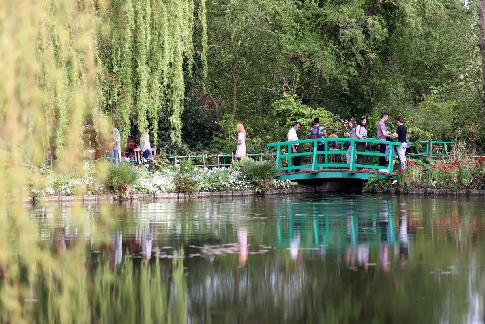 People walking over the iconic wooden bridge above the pond in Claude Monet’s gardens at Giverny
