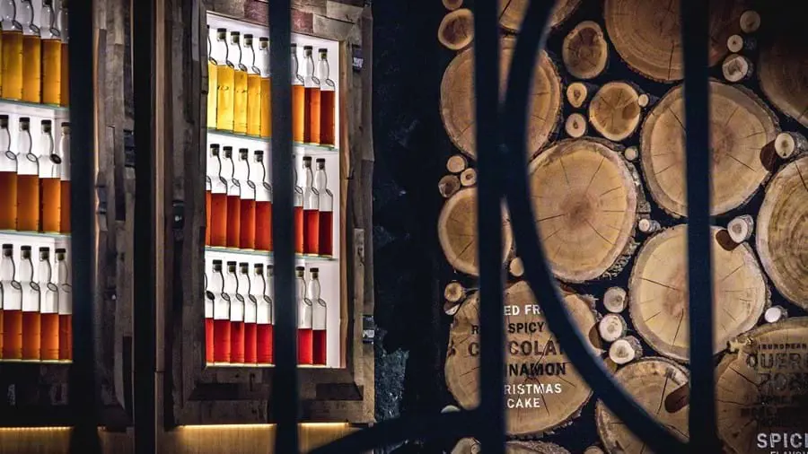 Malt whiskey bottles display in Glengoyne Warehouse with a wall of logs next to it