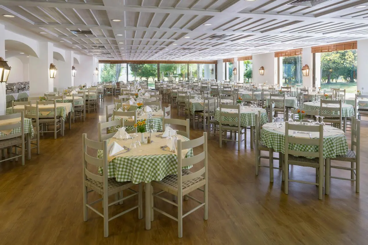 The bright dining room at Amalia Hotel, Olympia with wooden floors, green check tablecloths, and views of the garden