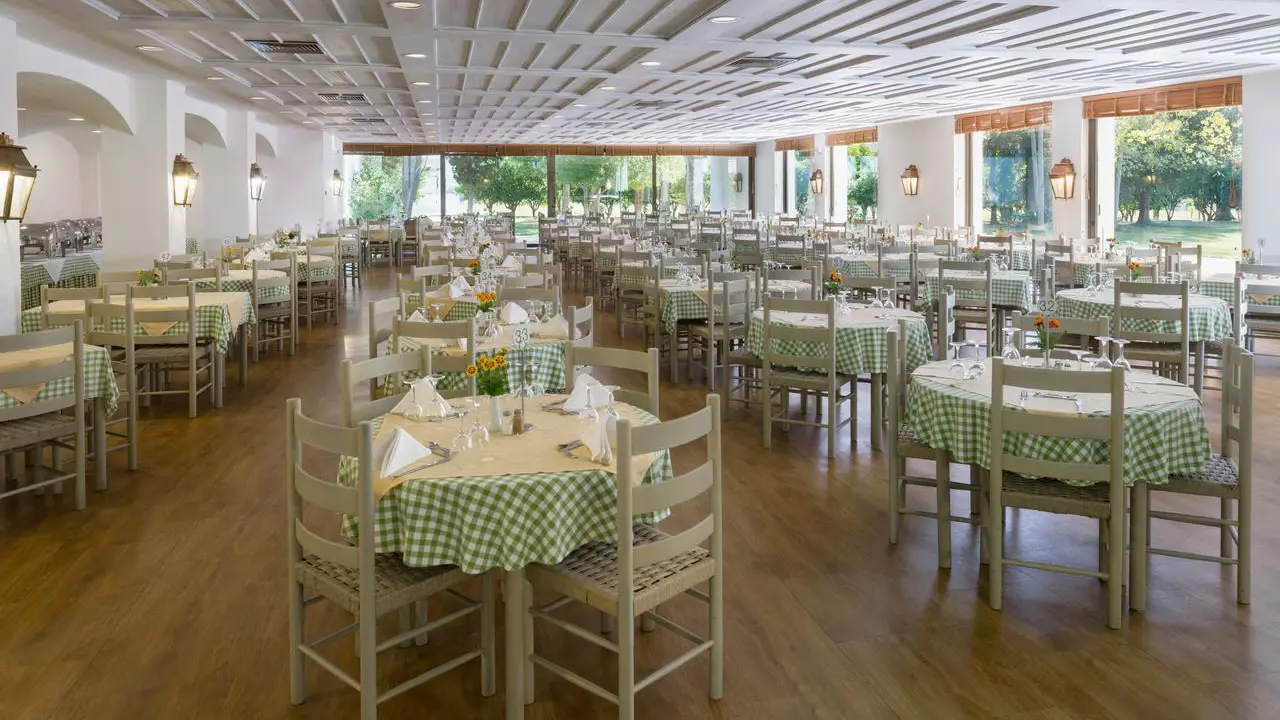 The bright dining room at Amalia Hotel, Olympia with wooden floors, green check tablecloths, and views of the garden