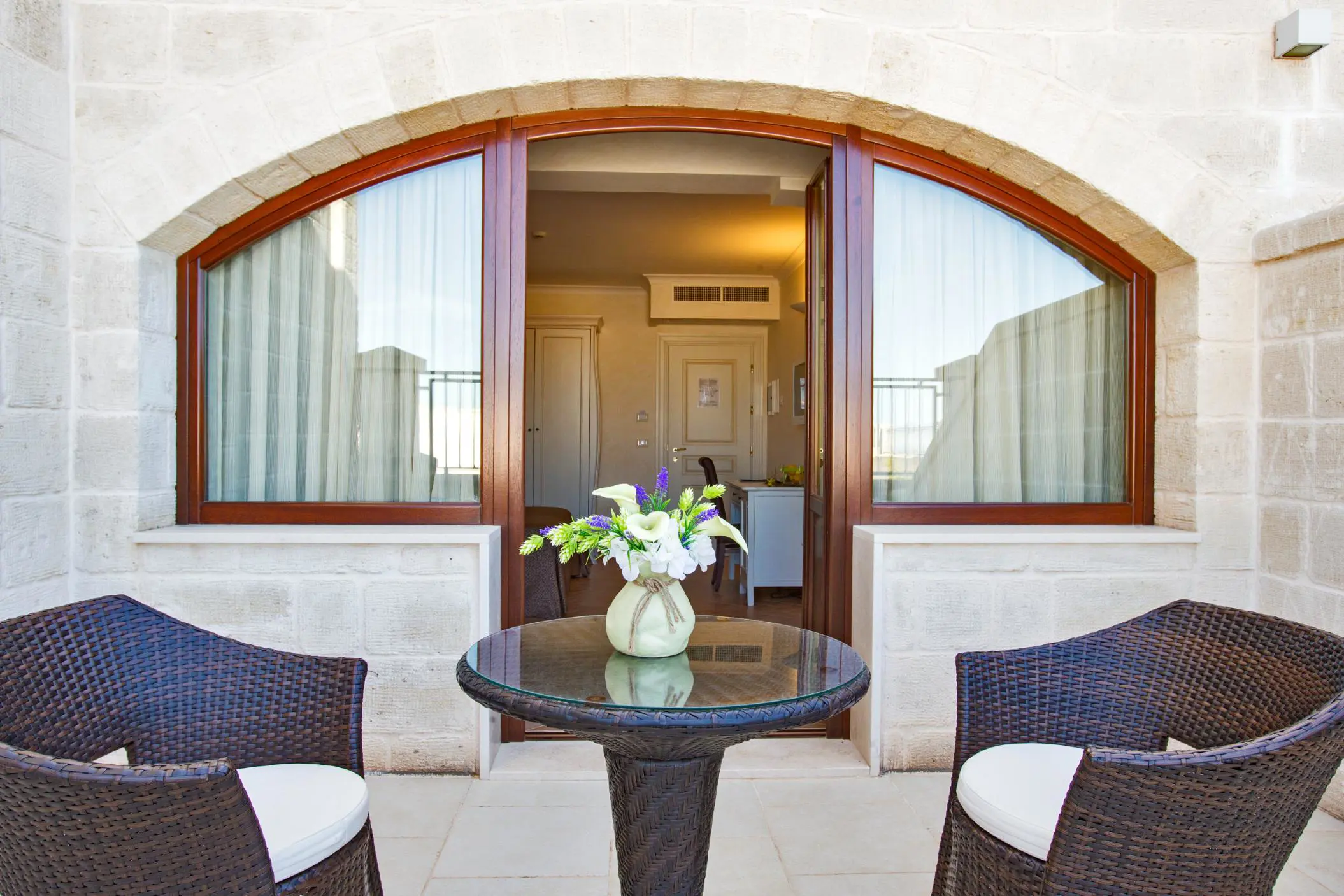 Private terrace at Masseria Caselli Hotel, Italy, with wicker chairs, a glass table, and a vase of fresh flowers