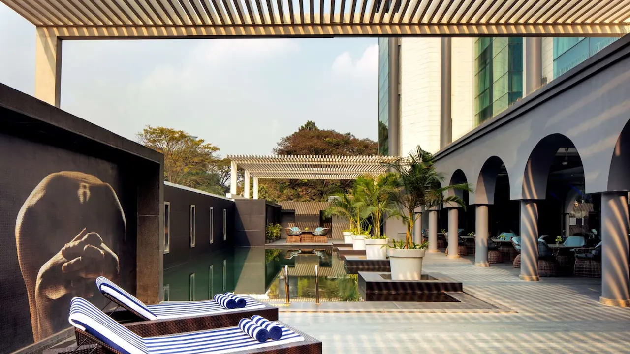 Outdoor pool on the terrace at Radisson Blu Atria in Bengaluru, with two sunbeds in the foreground, arched entrances to the interior terrace, and a covered lounge area visible at the far end
