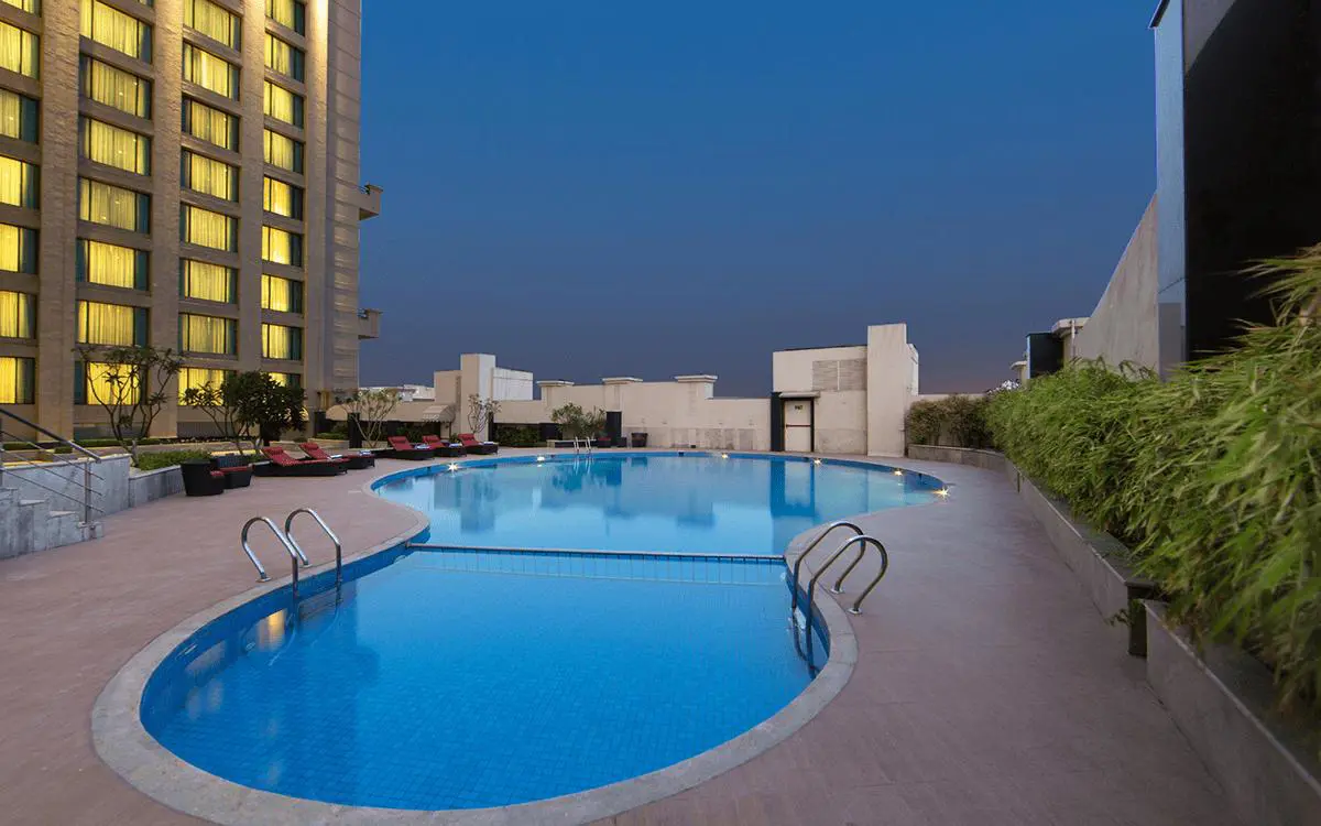 An outdoor swimming pool at WelcomHotel by ITC in Dwarka surrounded by sun loungers and greenery