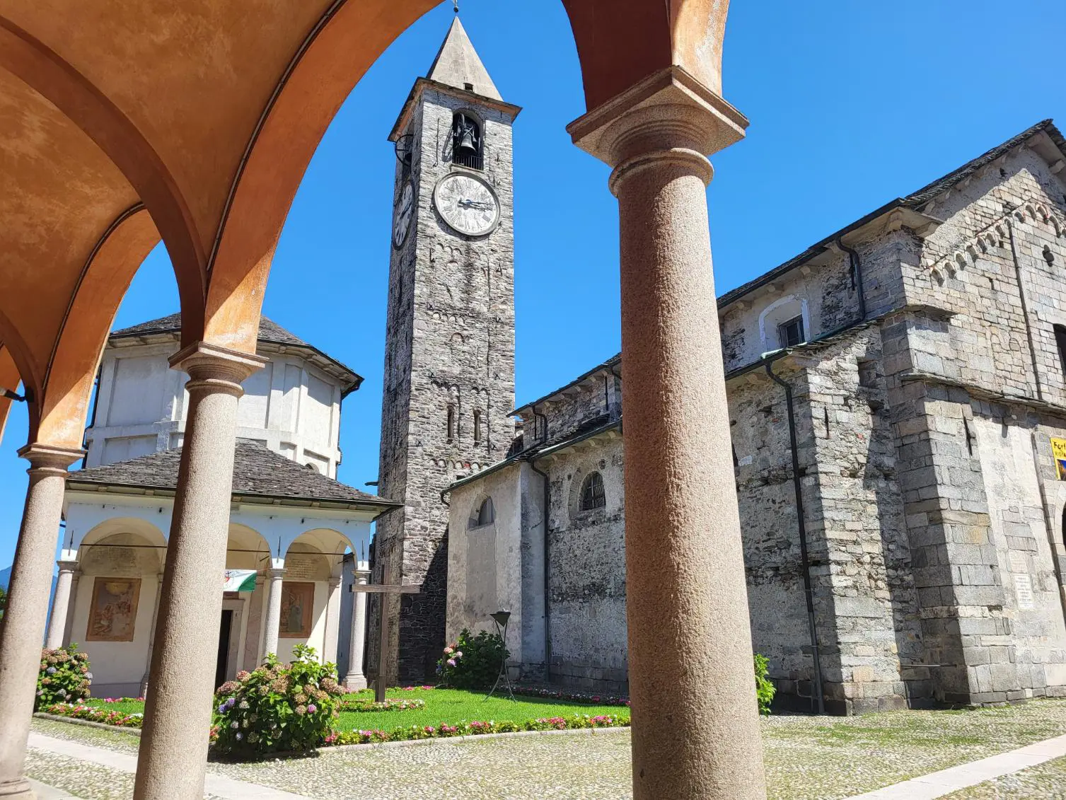 View of the Church of Gervasio and Protasio’s clock tower in Baveno, Italy, seen from under arches in the courtyard