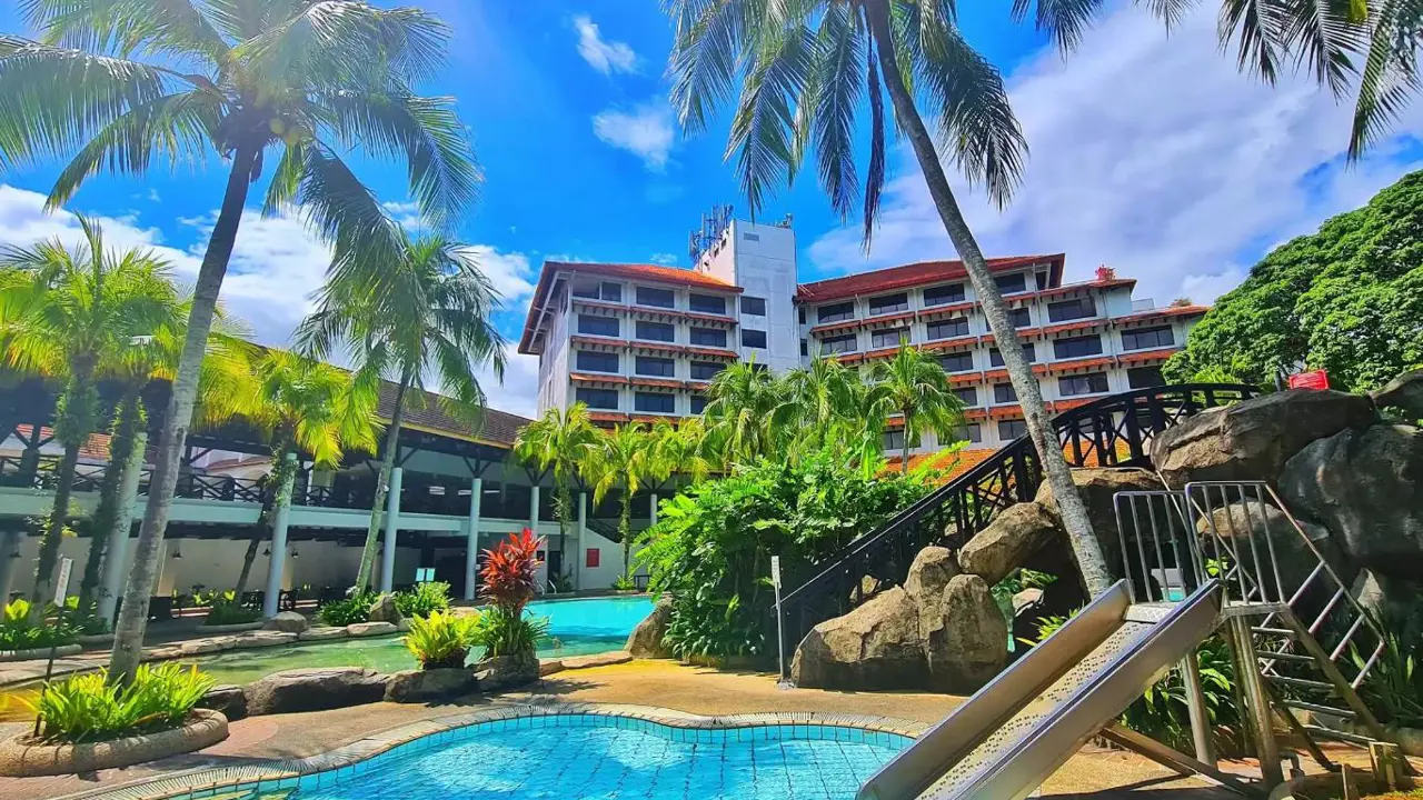 Two outdoor swimming pools at Sabah Hotel, Sandakan, with the hotel building in the background, surrounded by palm trees