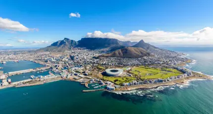Aerial view of Cape Town, South Africa, showing the city nestled between Table Mountain and the Atlantic Ocean, with the coastline, harbour, and urban landscape clearly visible
