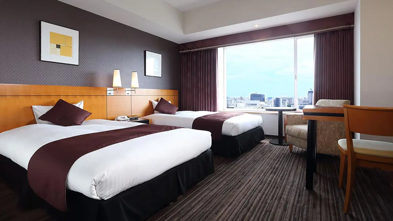 Contemporary twin hotel room at Hotel Nikko Ōita Oasis Tower, featuring two beds, large window with city views, and warm wooden furnishings