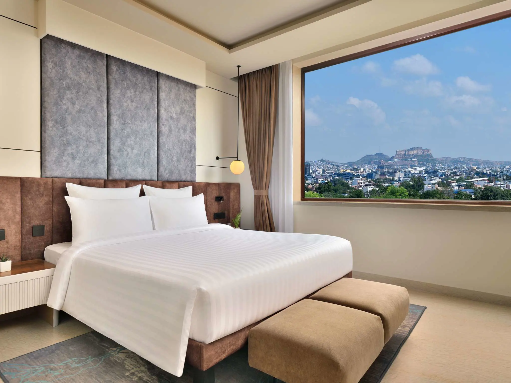 Bright guest room at Novotel Jodhpur with a king-size bed and large window offering city and fort views