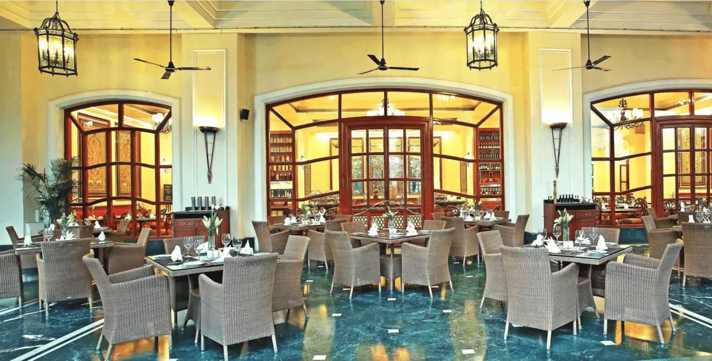 Elegant restaurant at Eros Hotel, New Delhi, with wicker chairs, set tables, and arched wooden windows