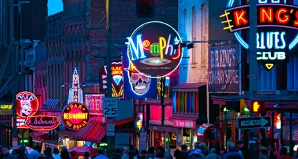 Vibrant night scene of Beale Street in Memphis, Tennessee, with colourful neon signs for bars, restaurants, and blues clubs, and a crowd of people walking along the street