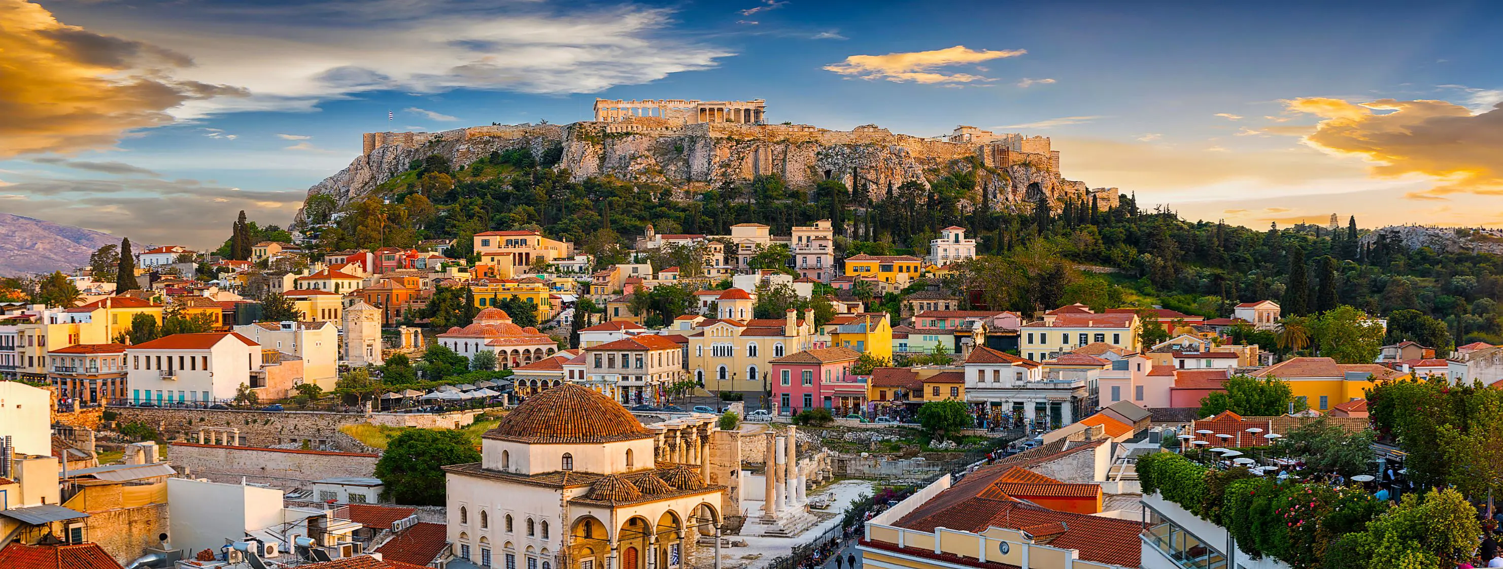 View of a city with colourful buildings and a rocky hill with ruins on the top.