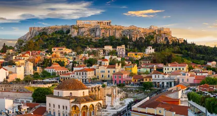 View of a city with colourful buildings and a rocky hill with ruins on the top.