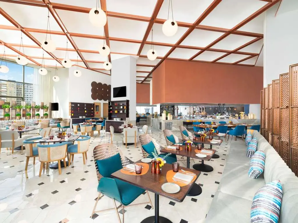Spacious restaurant with colourful seating, a high ceiling and large windows at the Novotel New Delhi City Centre