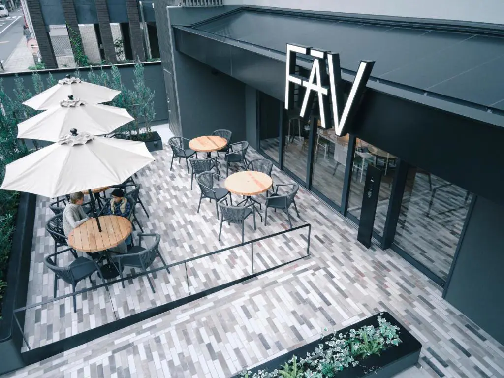 Outdoor terrace of FAV LUX Nagasaki with round tables, white umbrellas, and relaxed seating outside the entrance