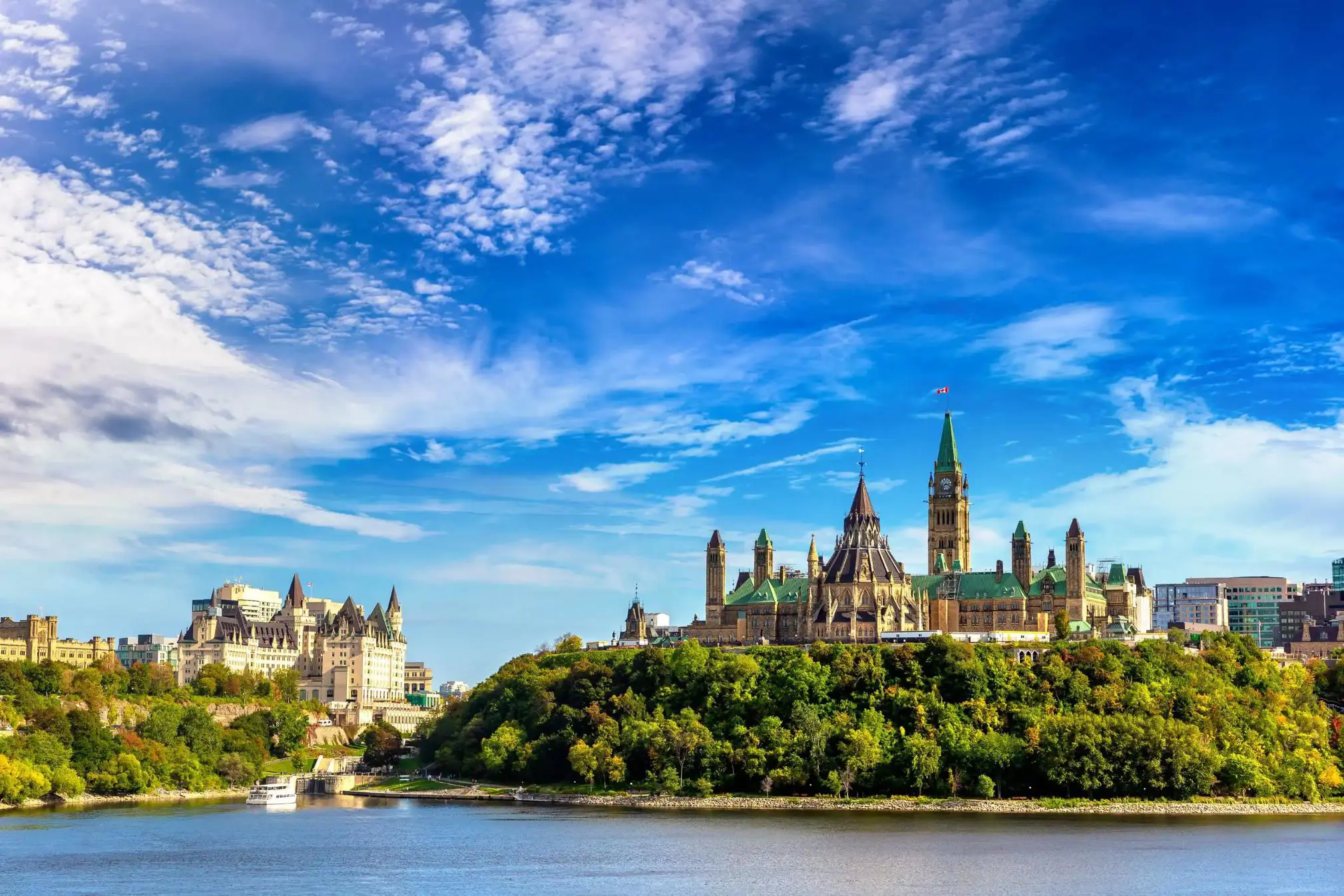 Ottawa skyline in Canada, showing Parliament Hill buildings above a river with trees in the foreground