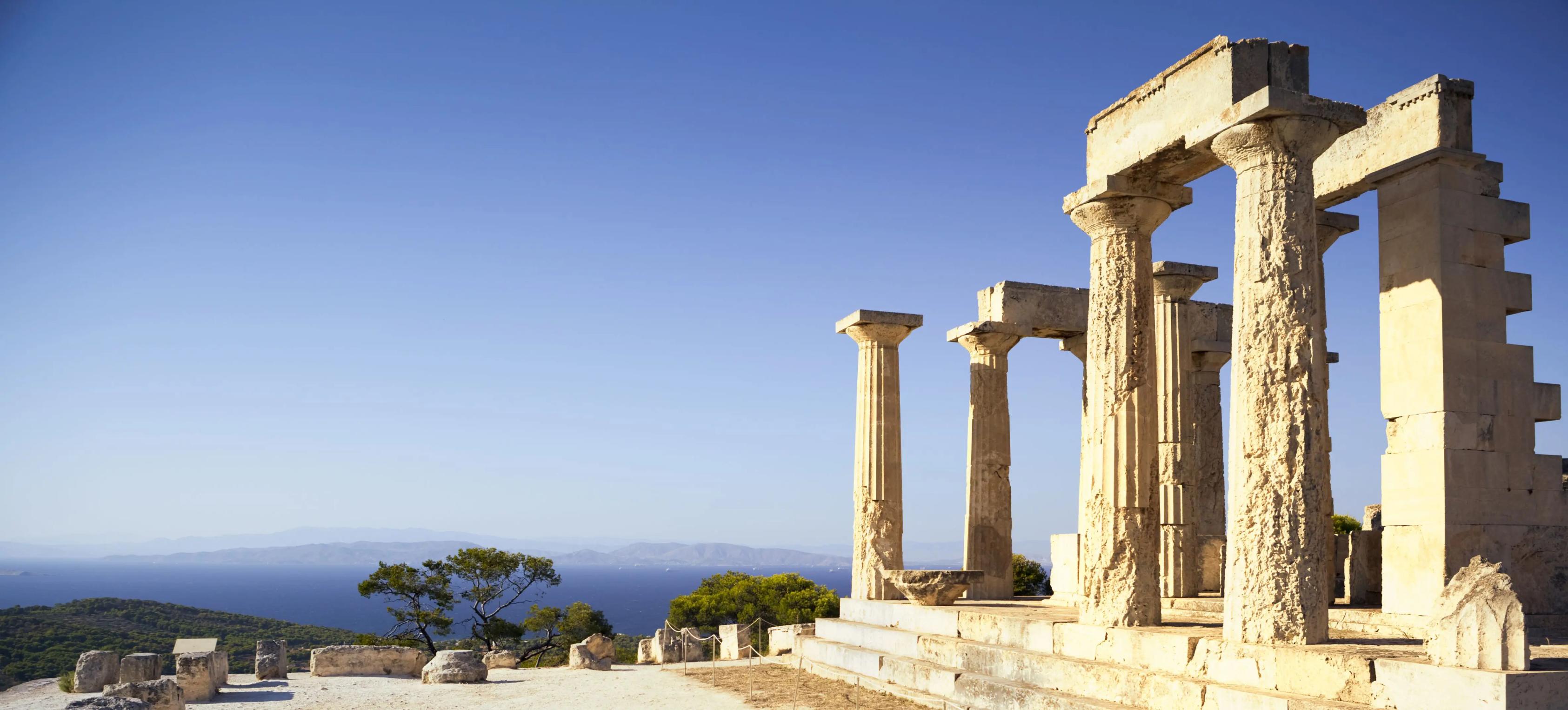 Ancient Greek temple ruins on an island with weathered stone columns overlooking the blue sea and distant mountains under a clear sky