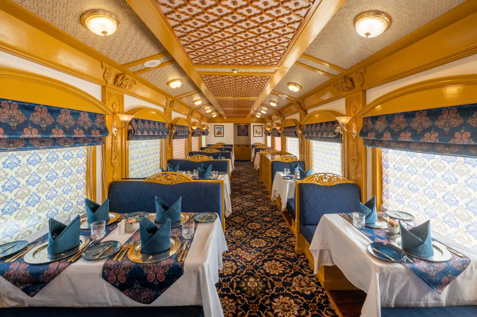 The Deccan Odyssey dining carriage, decorated with blue accents and patterns on the tablecloths, carpet, and window blinds