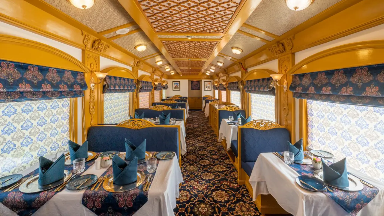 The Deccan Odyssey dining carriage, decorated with blue accents and patterns on the tablecloths, carpet, and window blinds