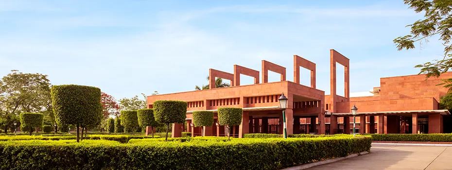 The grand red sandstone façade of Jaypee Palace in Agra surrounded by manicured hedges and trees under a clear sky