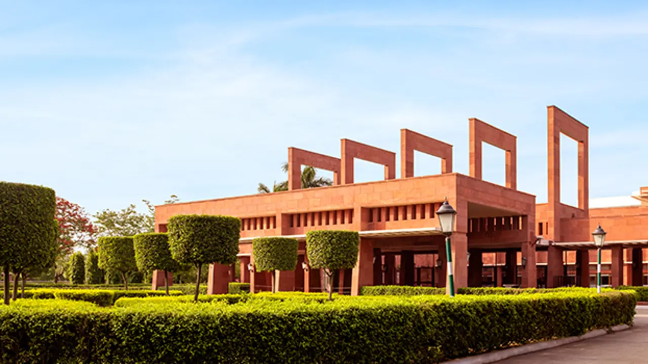 The grand red sandstone façade of Jaypee Palace in Agra surrounded by manicured hedges and trees under a clear sky
