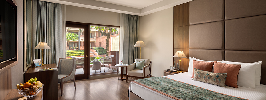 Elegant deluxe room at the Jaypee Palace in Agra with a king-size bed, soft lighting, and a private terrace overlooking lush gardens